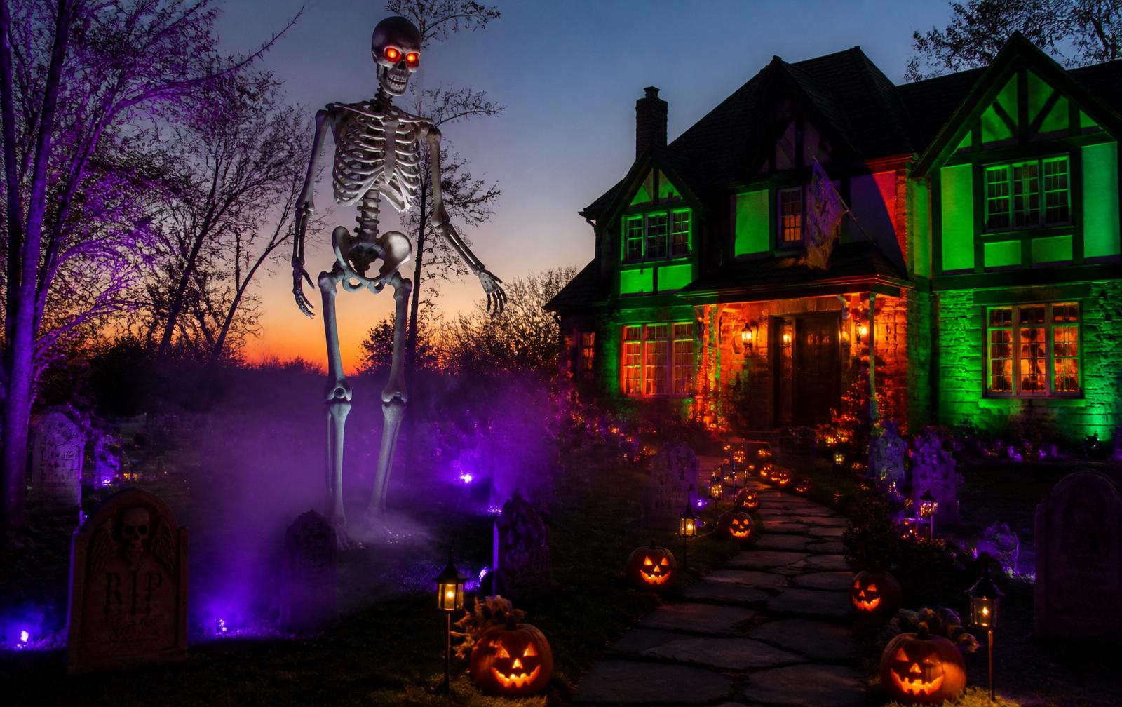 A twelve-foot skeleton looms over a Tudor home with purple fog and jack-o-lantern-lined path